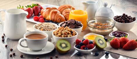 Une table de petit-déjeuner avec des croissants, des fruits, des céréales et du café.