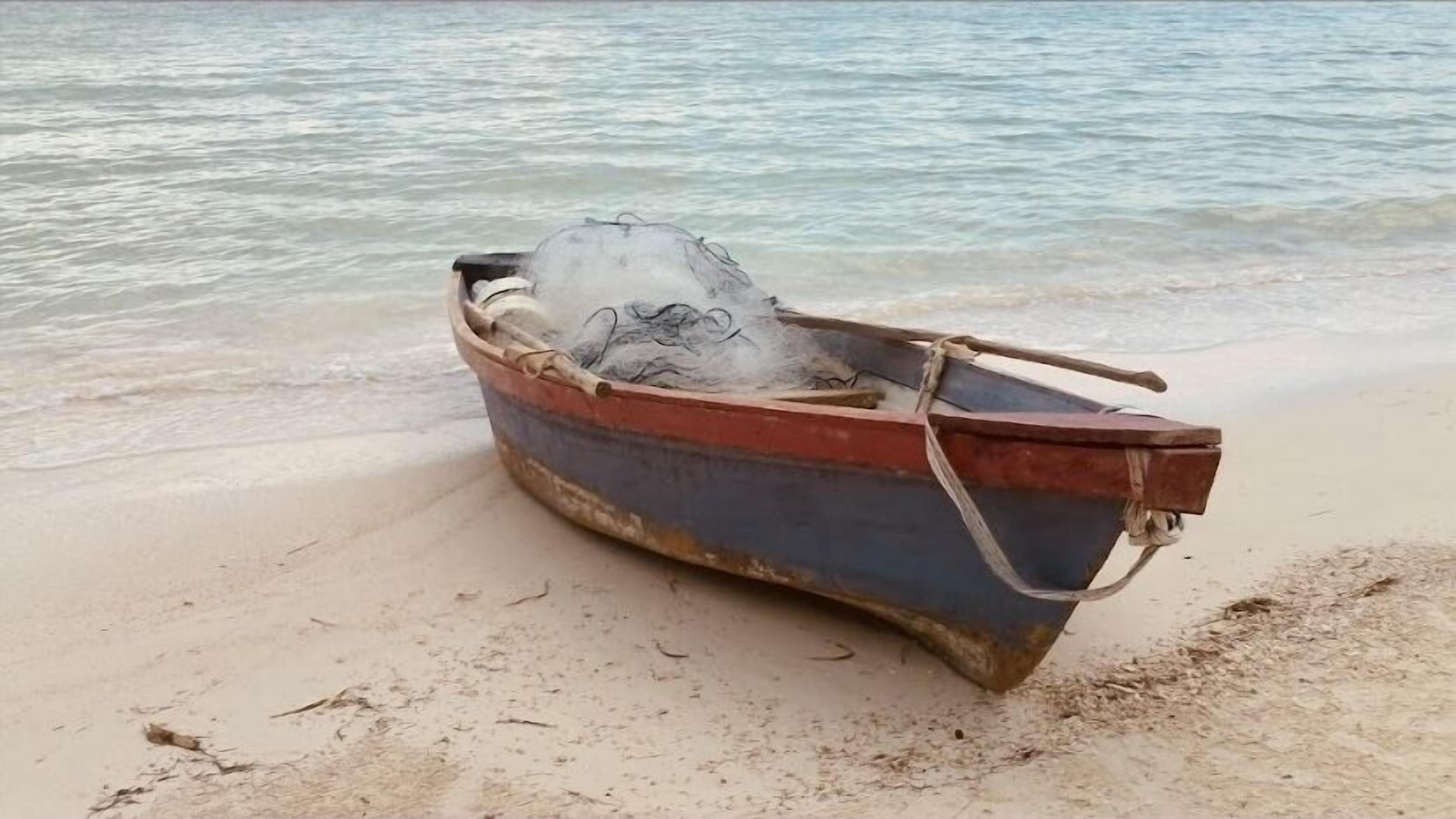 A small, weathered boat on a sandy beach near the water.