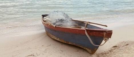 A small, weathered boat on a sandy beach near the water.