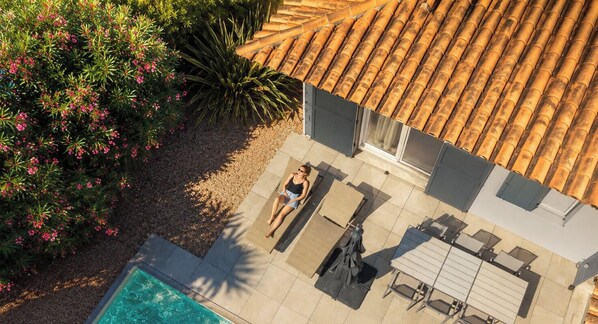 Une terrasse sur le toit avec une piscine, un espace détente avec une table et des chaises, et une vue sur le jardin et les bâtiments environnants.