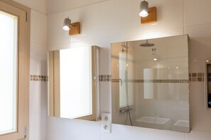 Une salle de bain avec un grand miroir, une douche et deux appliques murales.