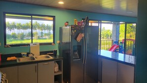A compact kitchen with a window offering a view of palm trees and a playground. - Rocas De Amancio Private Beachfront Estate (Puntarenas Province)