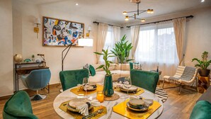 Een eetgedeelte met een ronde tafel voor vier personen, omringd door groene bekleden stoelen.