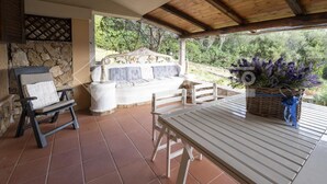 Eine überdachte Terrasse mit einer Steinwand, einem weißen Sofa, einem Tisch und einem Sessel.