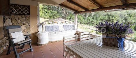 A covered patio with a stone wall, a white sofa, a table, and a chair.