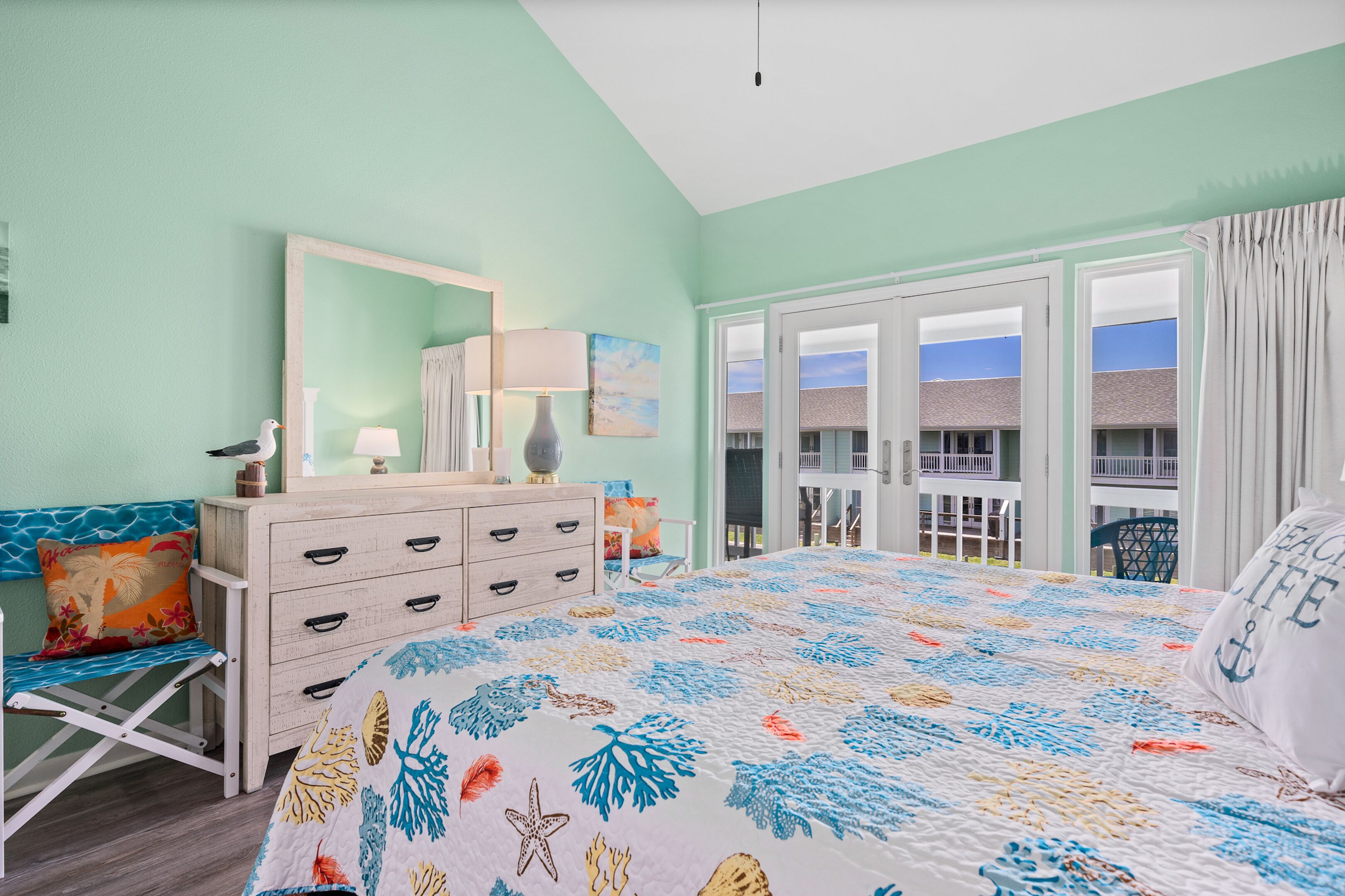 A bedroom with a bed, dresser, chair, and a view of the outside.