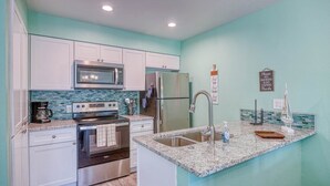 Een moderne keuken met witte kastjes, roestvrijstalen apparatuur, een granieten aanrechtblad en een turquoise achterwand.