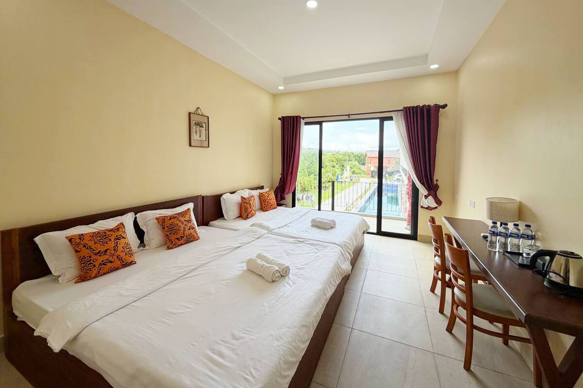 A hotel room with a large bed, a dining table with chairs, a view of the outdoors, and a water dispenser.
