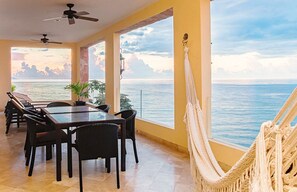 Un comedor con mesa y sillas, una hamaca y vista al mar.