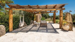Eine Terrasse im Freien mit einer Holz-Pergola, Steinmöbeln und einer Hängematte.