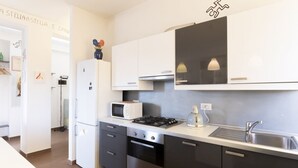 A modern kitchen with white cabinets, a built-in microwave, a gas stove, and a sink. - Casa del Maestro Apartment (Milano)
