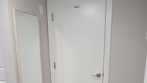 Una puerta blanca con una pequeña etiqueta, un espejo a la izquierda y un piso de madera claro.
