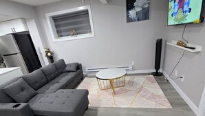 Una sala de estar moderna con un sofá seccional gris, una mesa de centro de mármol y un televisor de pantalla plana montado en la pared.