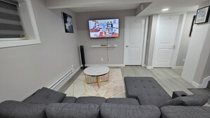 Una sala de estar moderna con un sofá seccional gris, una mesa de centro redonda y un televisor de pantalla plana montado en la pared.