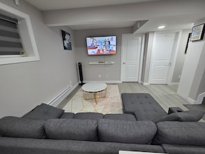 Una sala de estar moderna con un sofá seccional gris, una mesa de centro redonda y un televisor de pantalla plana montado en la pared.