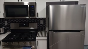 Una cocina moderna con electrodomésticos de acero inoxidable, incluyendo microondas, horno y refrigerador, con armarios blancos y un salpicadero hexagonal negro.