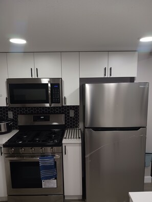 Una cocina moderna con electrodomésticos de acero inoxidable, incluyendo microondas, horno y refrigerador, con armarios blancos y un salpicadero hexagonal negro.