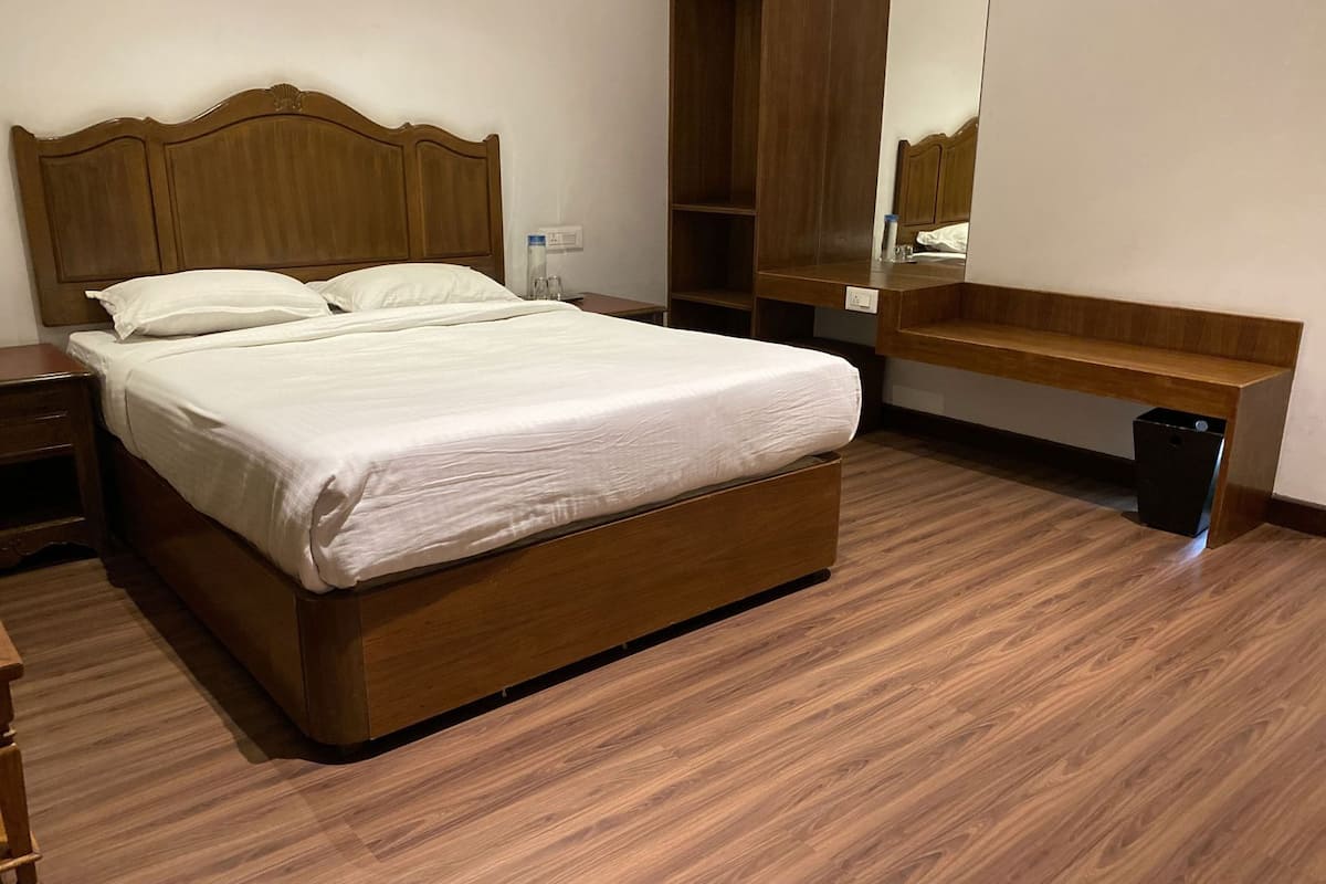 Ein ordentlich gemachtes Bett in einem Hotelzimmer mit einem hölzernen Kopfteil, einem Nachttisch, einer kleinen Ablagefläche und einer Mülleimer.