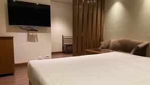 A hotel room with a large bed, a television mounted on the wall, a wooden chair, and a wooden partition. - Hotel Glanton Manor (Ootacamund)