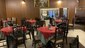 A restaurant with round tables covered in red tablecloths, wooden chairs, and a wooden paneled wall with a painting. - Hotel Glanton Manor (Ootacamund)