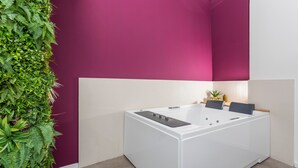 A modern bathroom with a white bathtub, a green vertical garden, and a purple accent wall.