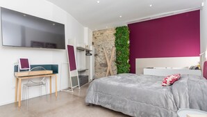 A modern bedroom with a bed, a desk, a TV, and a stone wall.