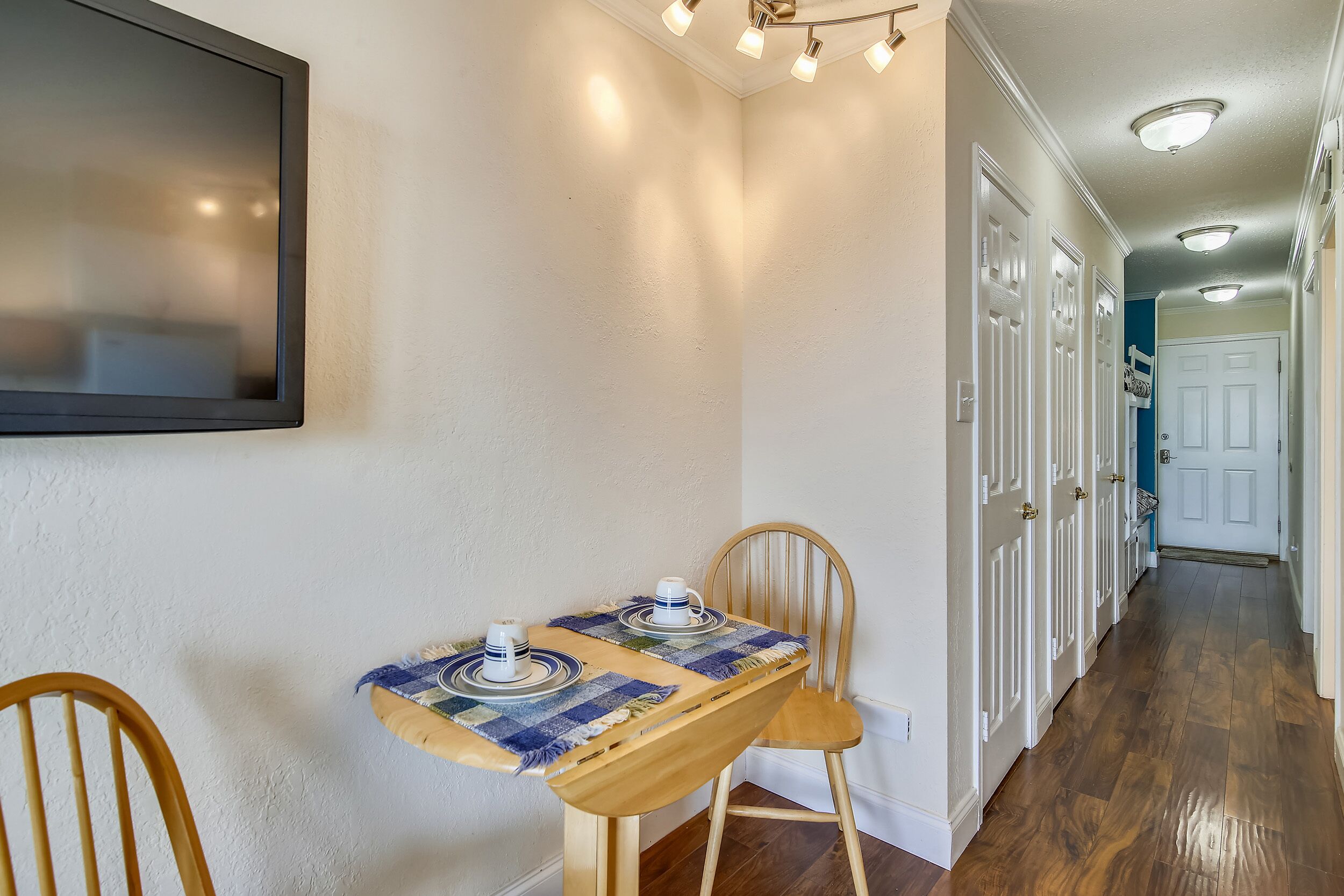 A hallway with a wooden dining table set with plates and cups, a chair, and a wall-mounted TV.