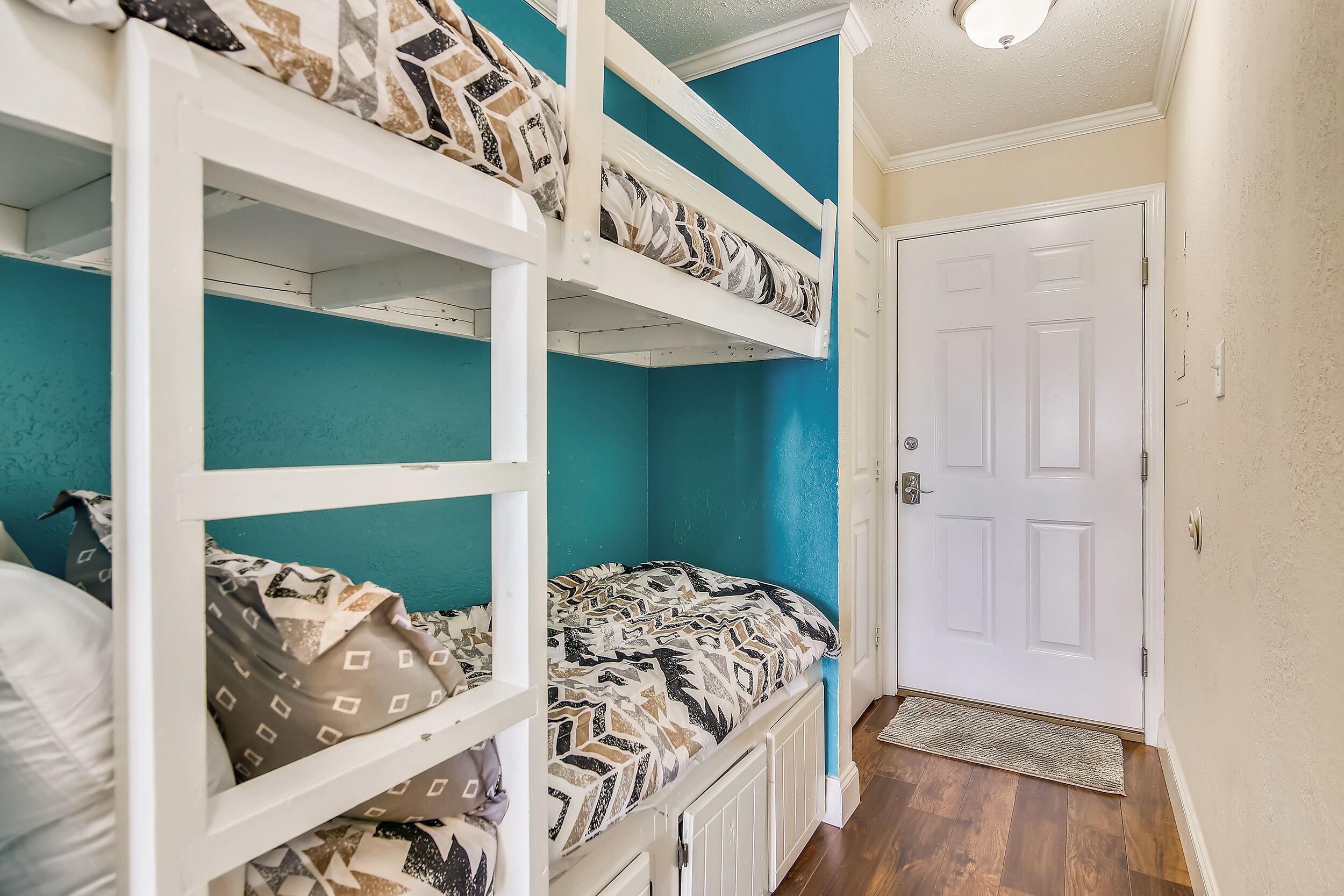A room with bunk beds, a white door, and a teal accent wall.