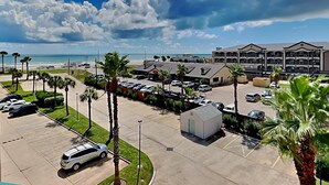 A hotel with a parking lot, a beach view, and a building with multiple balconies. - Casa Del Mar by Ryson Vacation Rentals (Galveston)