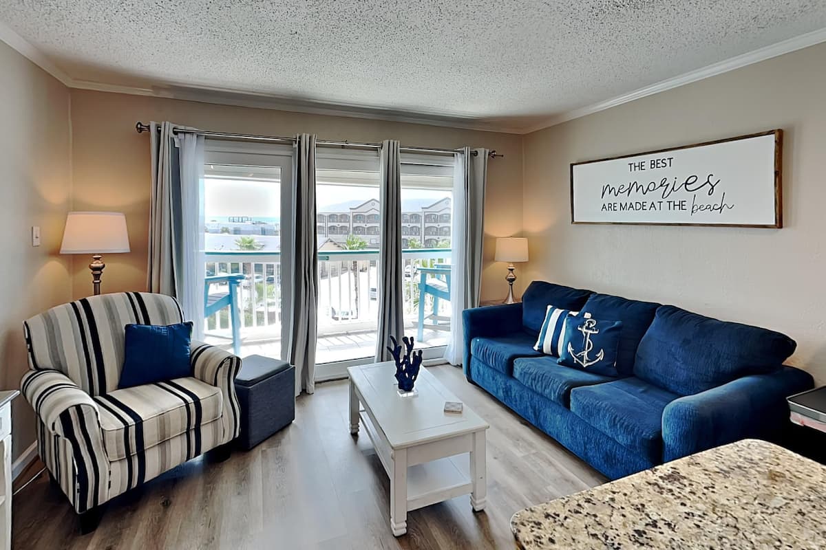 A living room with striped and blue sofas, a white coffee table, and a view of the beach through large windows.