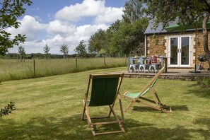 A grassy outdoor area with a wooden chair and a small building with a stone facade and a glass door.