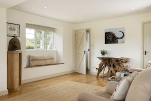 A spacious living room with a wooden floor, a sofa, a coffee table, a window with a view, and a door leading to another room.
