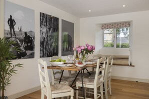 Un espace repas avec une table en bois, des chaises blanches et des œuvres d’art accrochées aux murs.