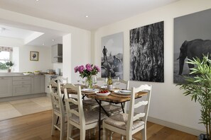 A dining area with a wooden table, white chairs, and a vase of flowers. There are three black and white photographs on the wall.