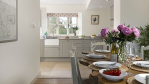A modern kitchen with a dining area, featuring a large window, a map on the wall, and a table set for dining. - Pet Friendly Rural Cotswold Cottage - 1 Manor Farm Cottage (Hook Norton, Banbury)