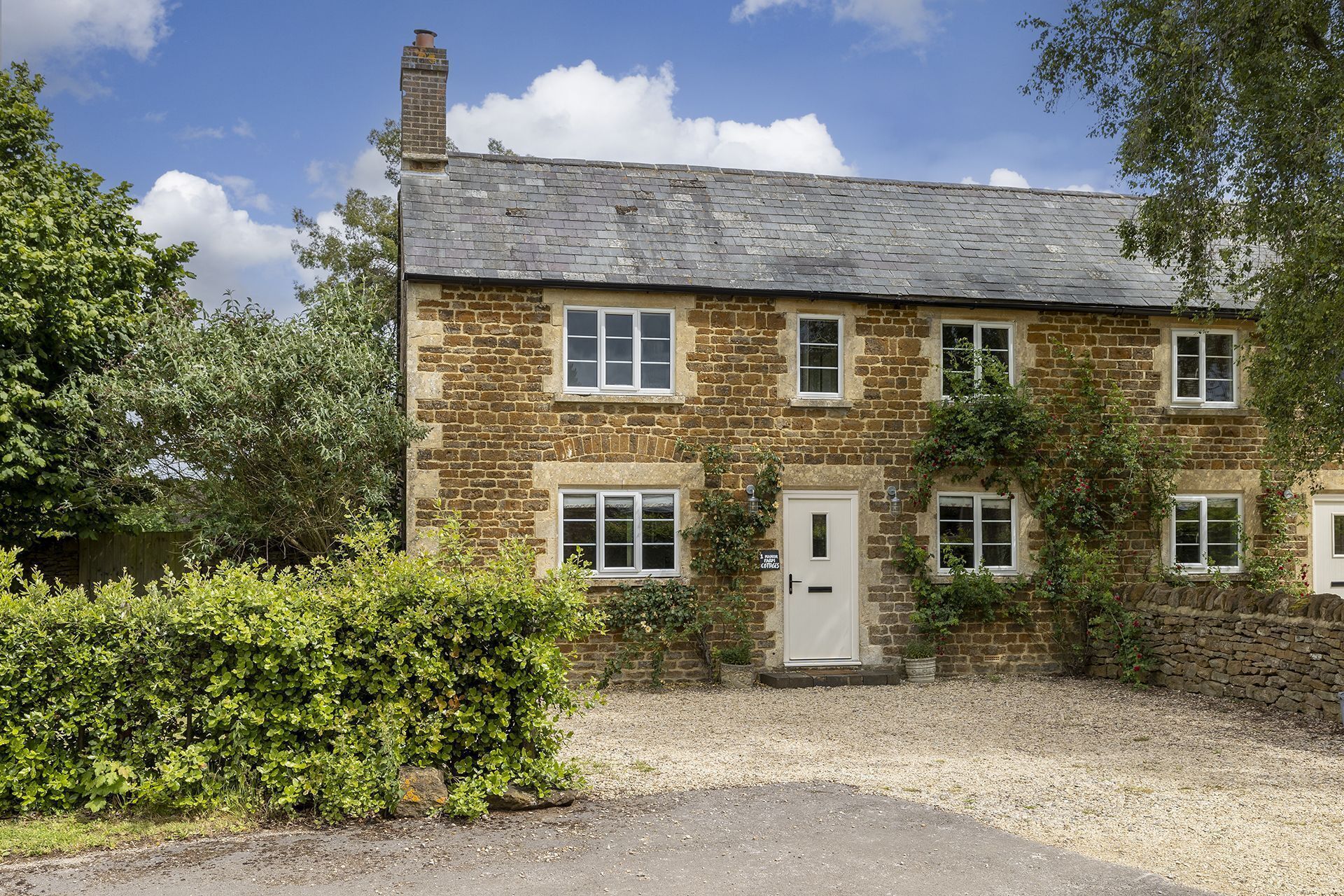 Une maison en pierre avec une allée en gravier et un petit jardin.