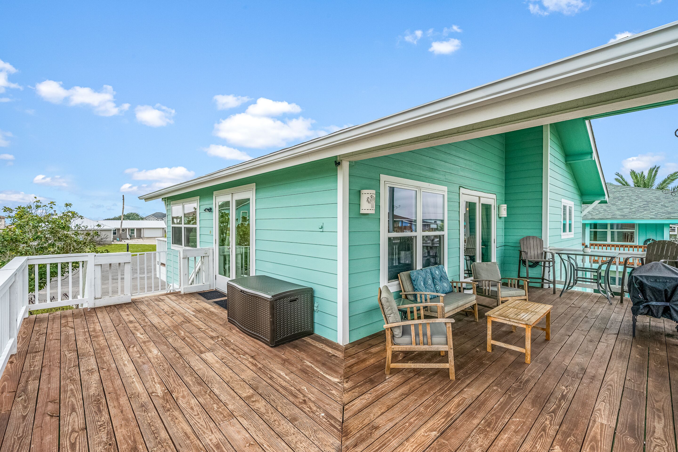 A turquoise house with a wooden deck, outdoor seating, and a covered area with a table and chairs.