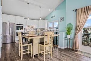 Una cocina moderna con armarios blancos, electrodomésticos de acero inoxidable y una mesa de comedor de madera con sillas.