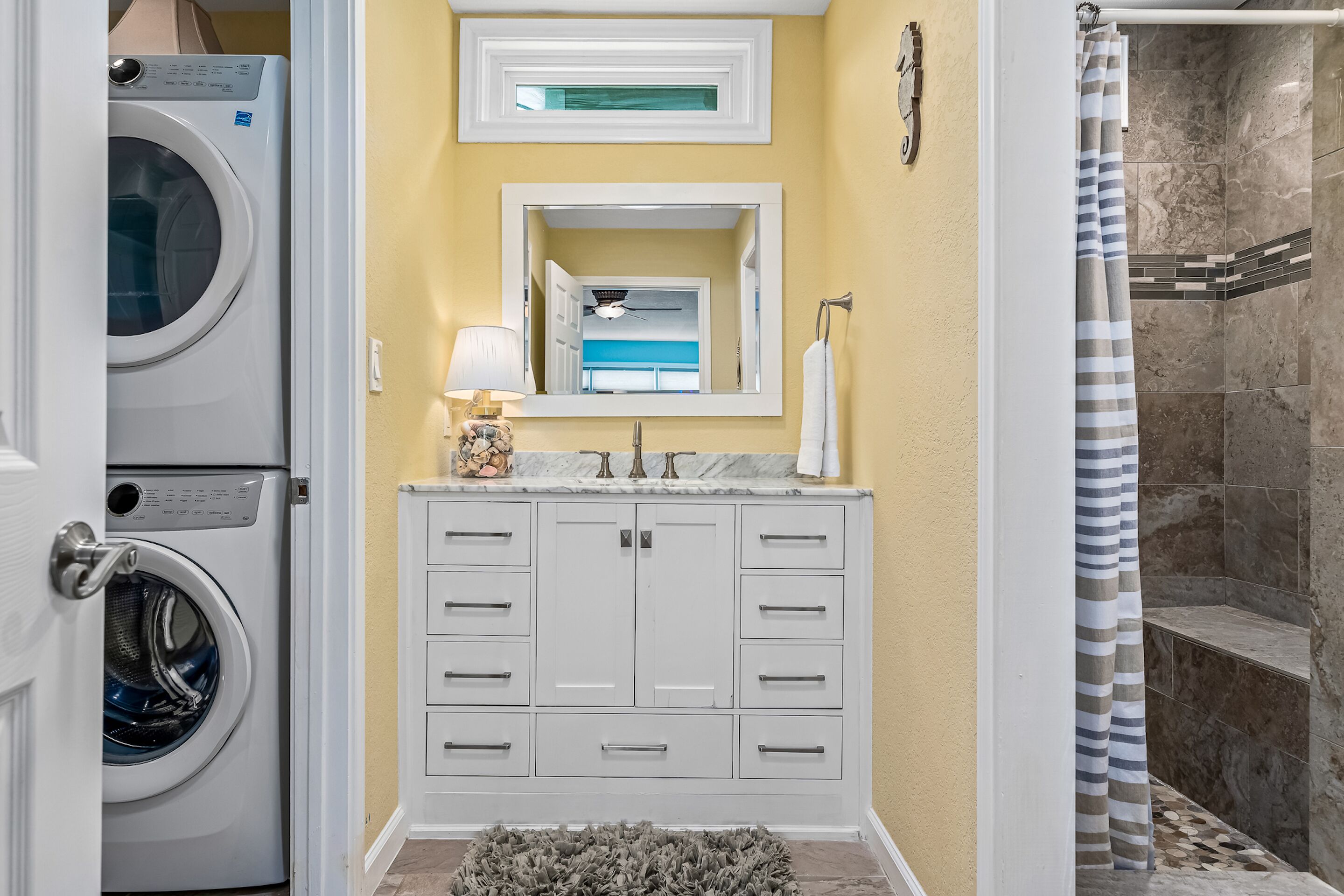 A compact bathroom with a washing machine, a sink with a mirror, and a shower area.