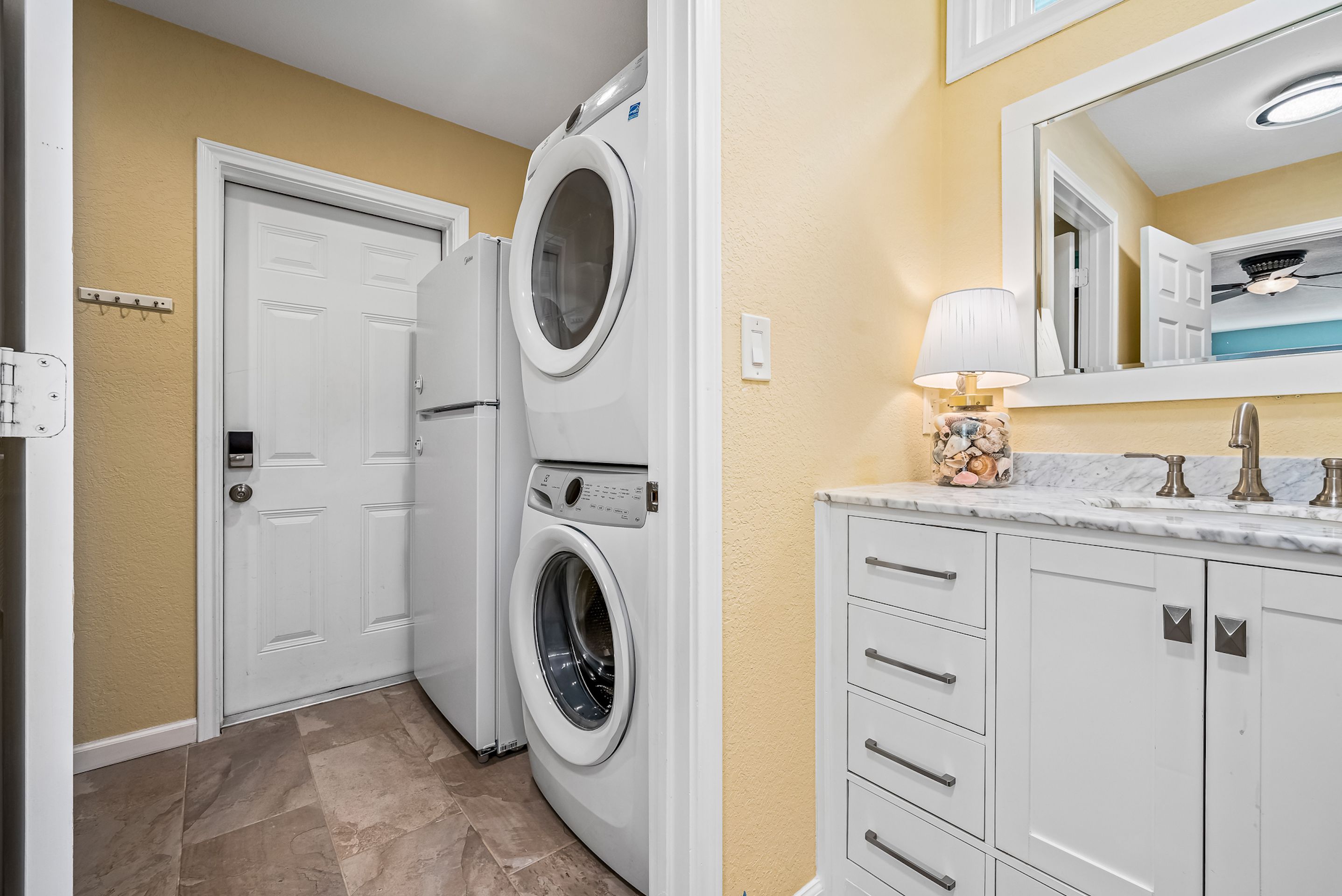 A laundry room with two stacked front-loading washing machines, a white door, and a vanity with a mirror and sink.