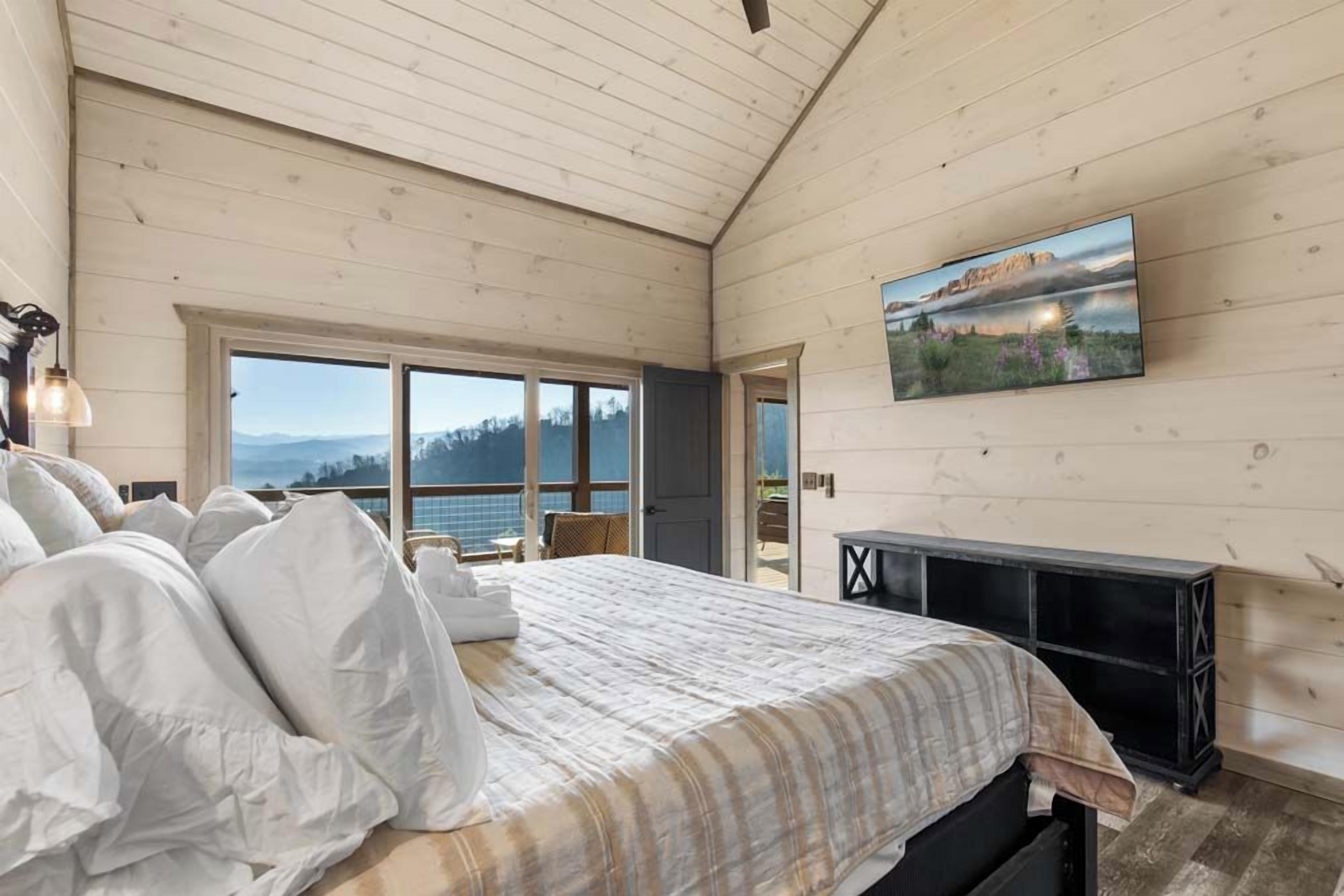 Un dormitorio con una cama grande, televisión y vistas a las montañas a través de la ventana.