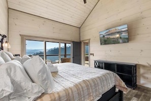 Un dormitorio con una cama grande, un televisor y vistas panorámicas a través de las ventanas.