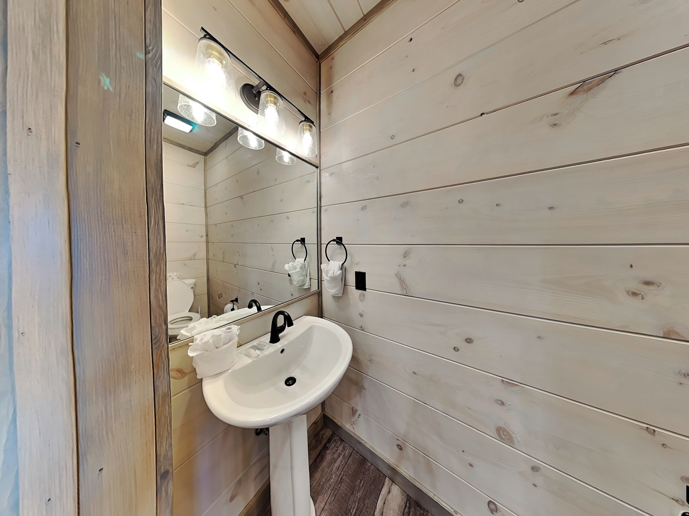 Ein Badezimmer mit einem weißen Waschbecken, einem Spiegel und einer Holzwand.