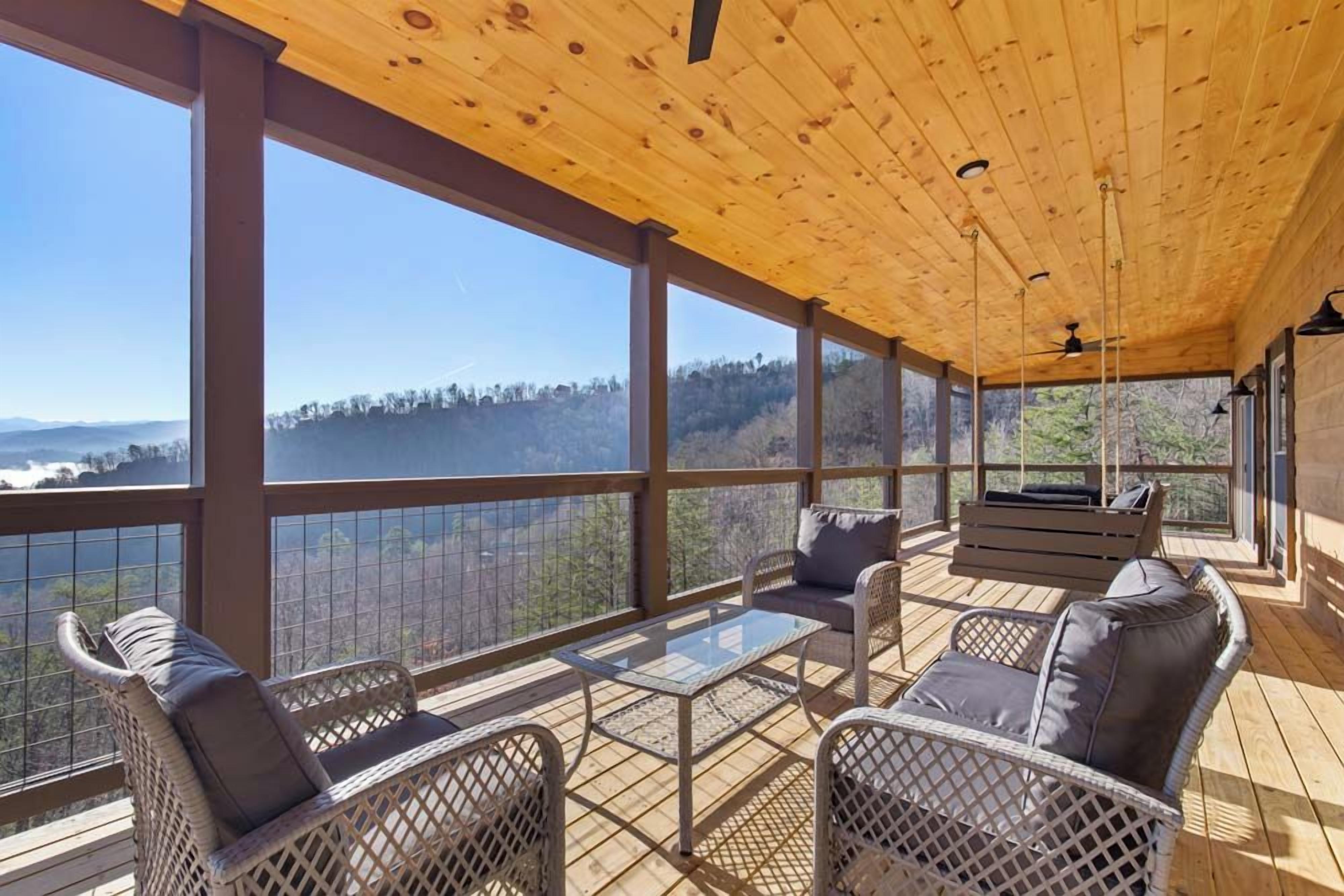 A covered outdoor seating area with wicker furniture and a glass table, overlooking a mountainous landscape.