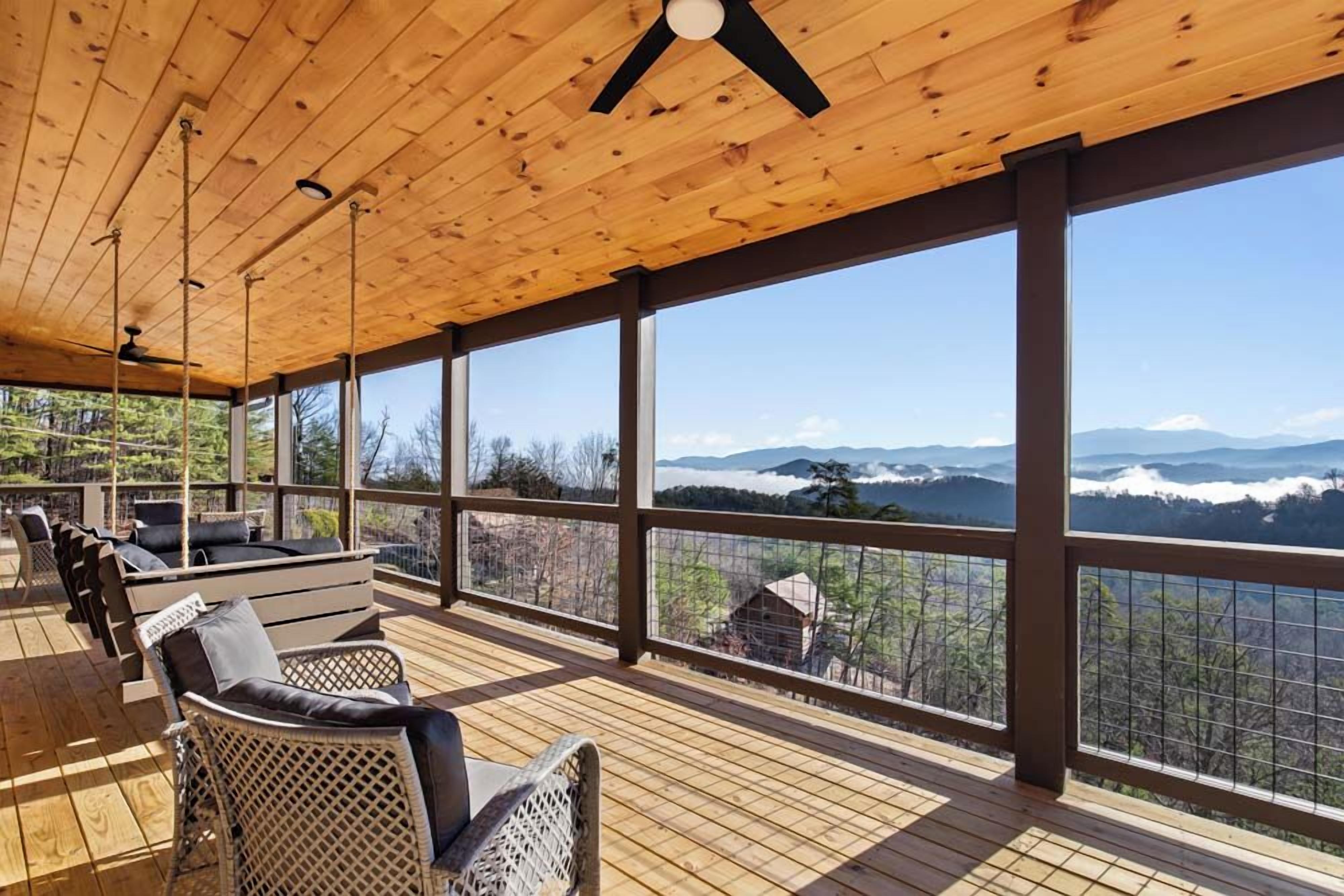 Un espace extérieur aménagé, abrité et doté d’un plancher en bois et de grandes fenêtres offrant une vue sur les montagnes.