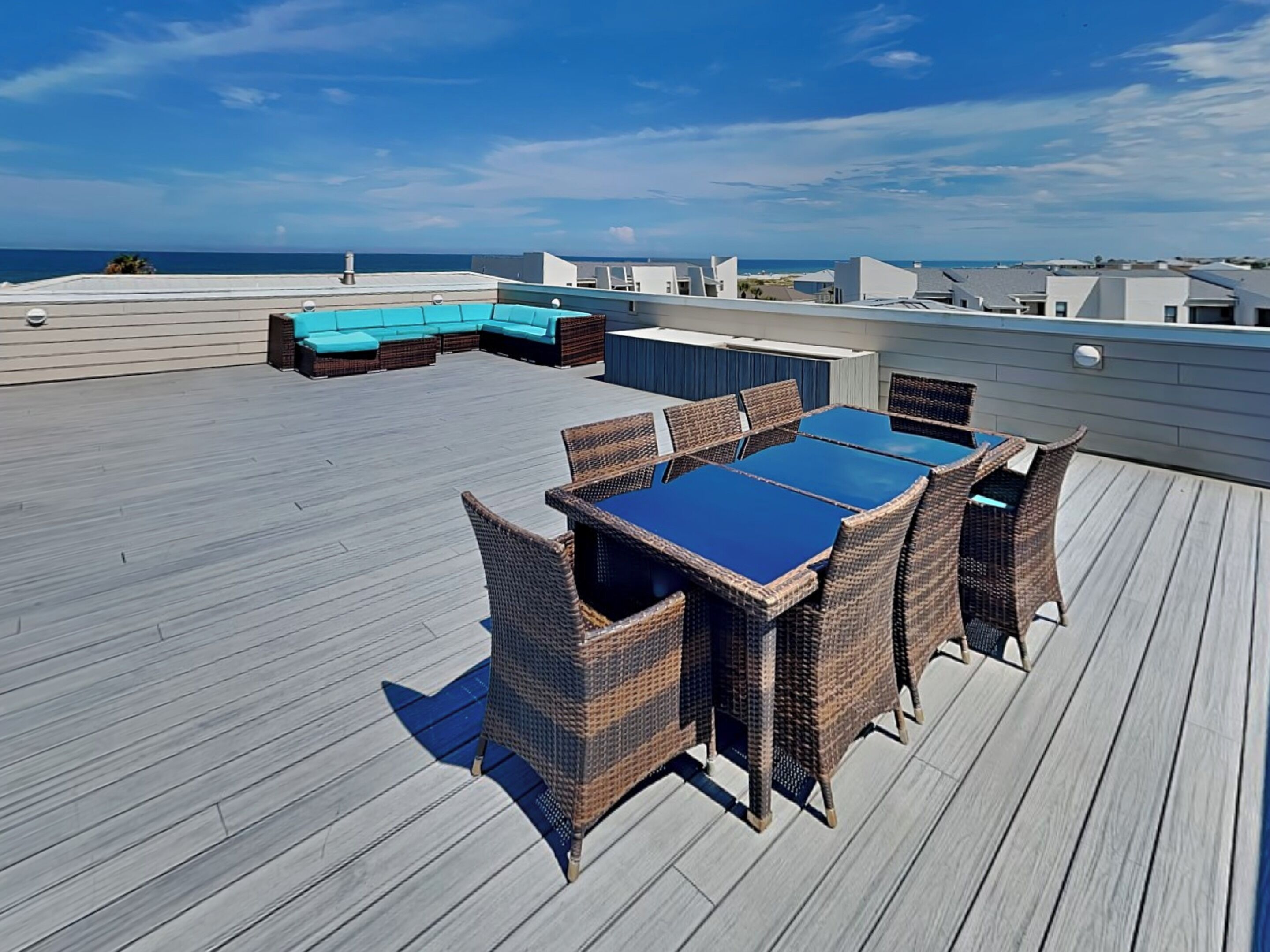 A rooftop deck with a dining area featuring wicker furniture and a blue table.