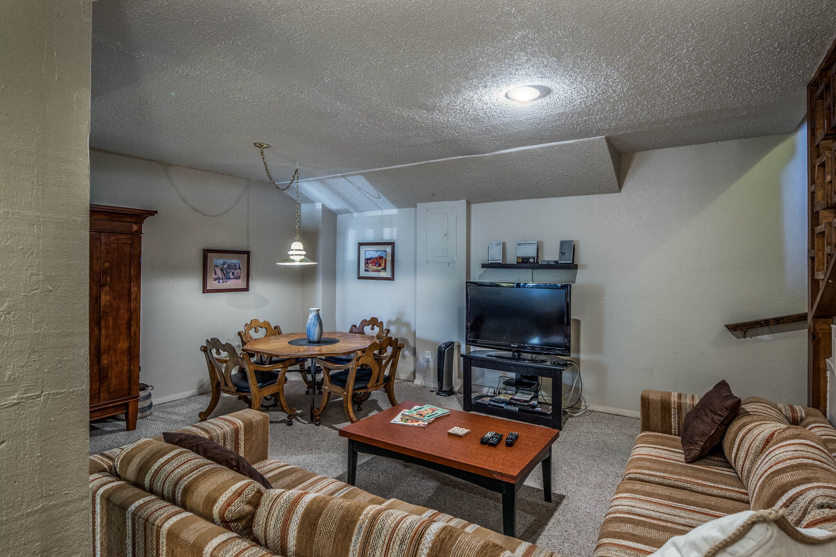 A living room with a sofa, a coffee table, a TV, and a dining area with chairs and a table.