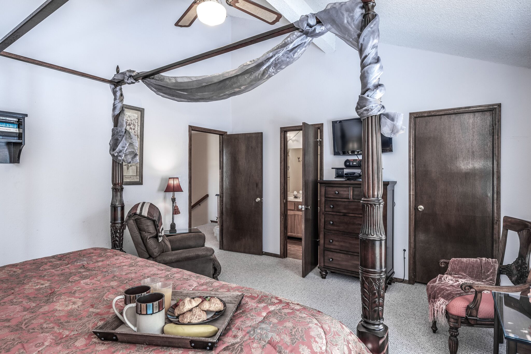 A bedroom with a four-poster bed, a tray with breakfast items, a television, and a wardrobe.