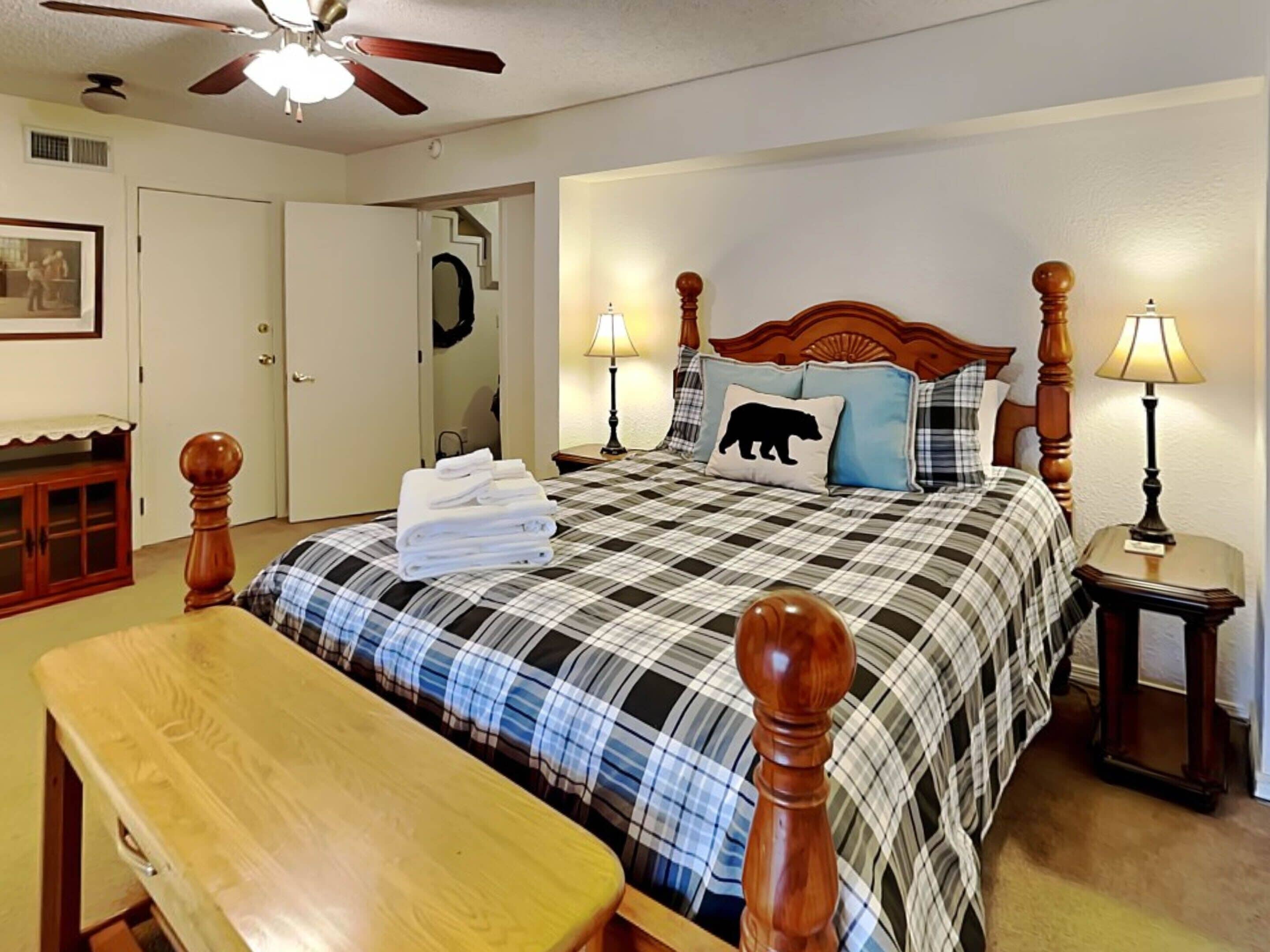 A neatly arranged bedroom with a bed, bedside lamps, a wooden bench, and a ceiling fan.