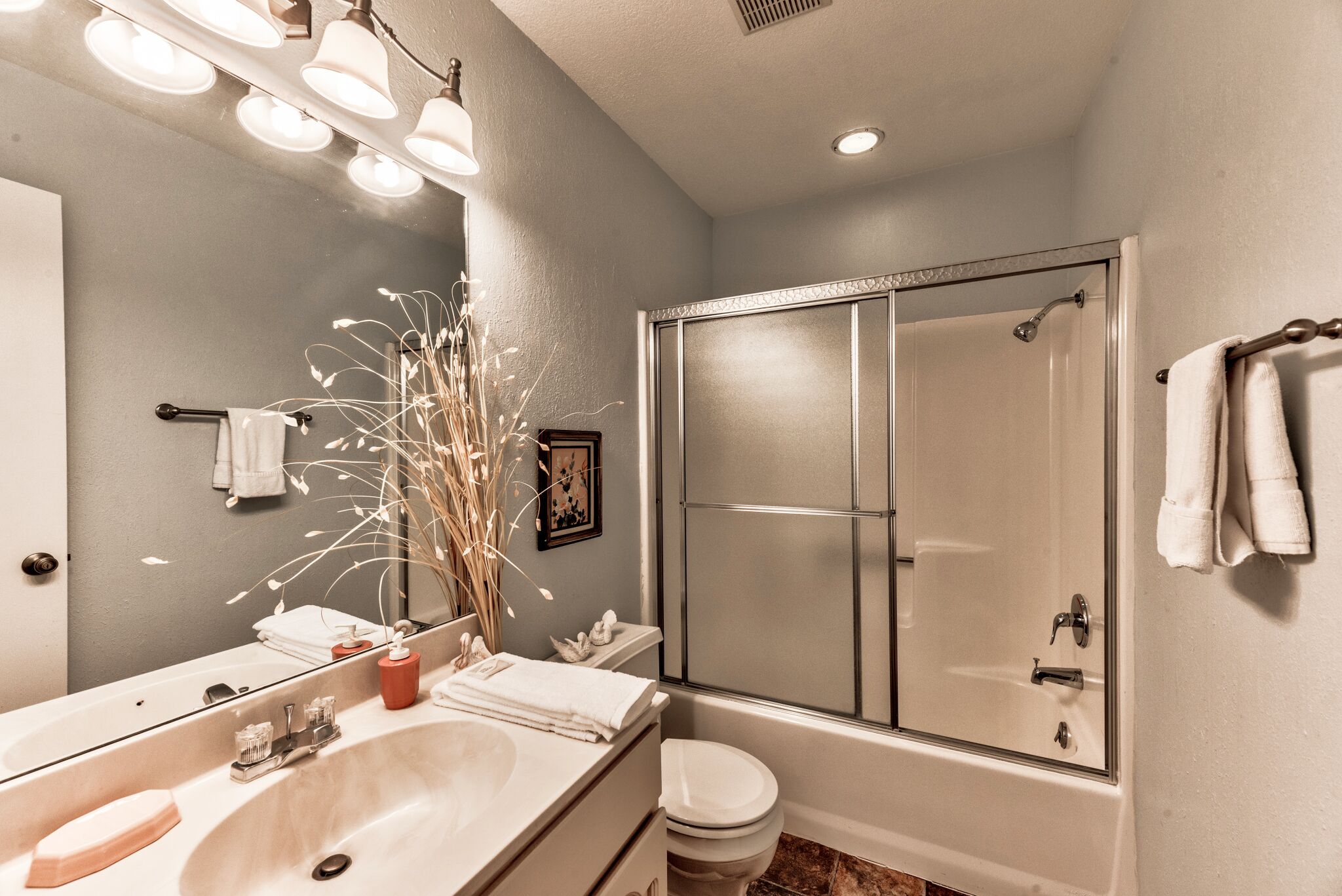 A bathroom with a large mirror, a sink, a toilet, and a shower.